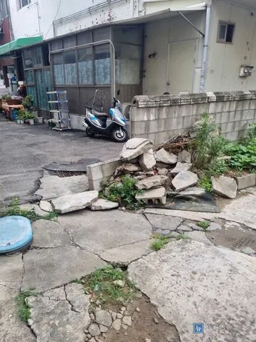 균열과 파손이 심한 주차장 입구 콘크리트 바닥과 쌓여 있는 석재 조각