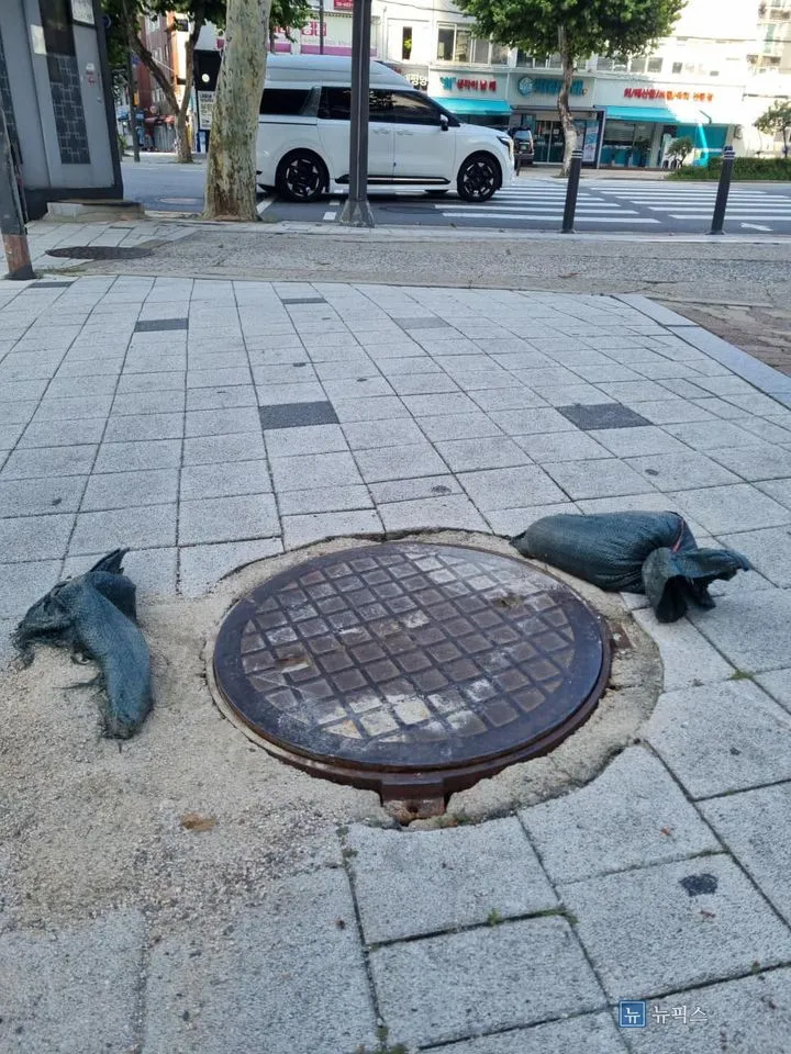 상가 앞 인도에 설치된 녹슨 맨홀뚜껑과 주변 보도블럭