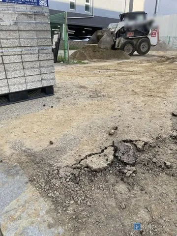 아스콘이 깨져 잔자갈이 흩어진 주차장 입구 진입로와 적재된 보도블럭 자재