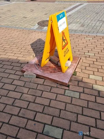 보도블럭보다 솟아오른 맨홀뚜껑 위에 안전표지판이 세워진 작업 전 모습