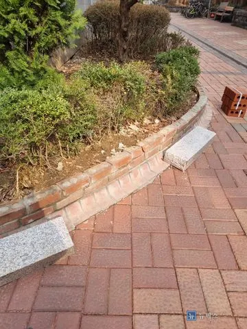 상단 벽돌이 깨져 나간 아파트 화단 담장과 보도블럭 위에 놓인 화강석 블록